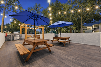 A wooden picnic table is set up under a blue umbrella on a wooden deck.